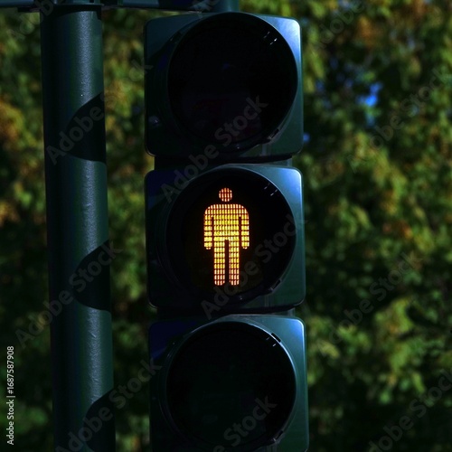 A close-up view of a traffic light for pedestrians displaying a yellow illuminated walking figure, indicating a warning or transition phase