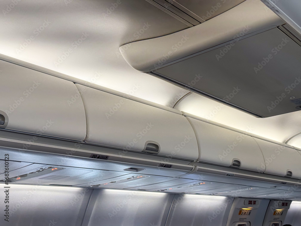 Fototapeta premium Overhead luggage compartments and cabin ceiling inside a passenger airplane. Travel, aviation, and the practical design of space in modern aircraft cabins.