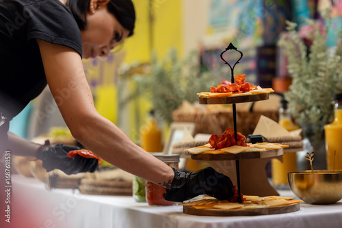 Quadro su tela Professional caterer wearing black gloves arranging charcuterie board with artis