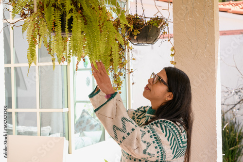 Woman wearing a Christmas sweater tending to the plants in her garden, fern