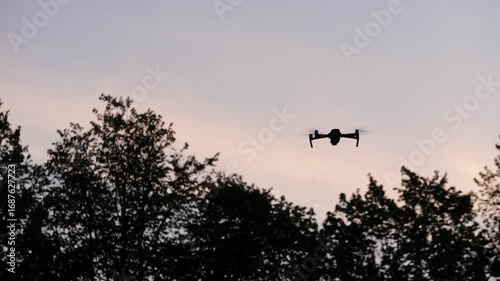 The silhouette of a drone hovering in the air against the backdrop of dark trees