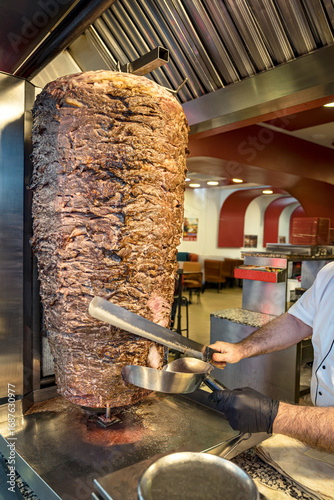 Close up of a huge spinning meat top called in Turkish “Doner Kebab”.
Slicing lamb or beef meat from the rotating heap of stacked and broiled meat.