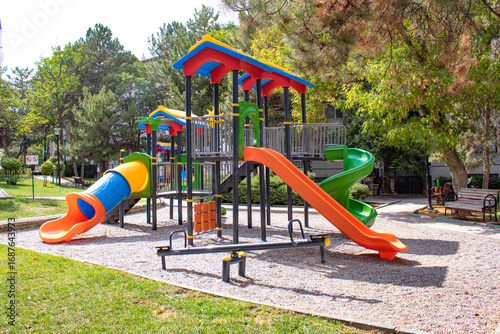 Bright plastic playset with tunnel slide, spiral slide and seesaw in a green park. Useful for education, recreation, childcare brochure, urban planning article, parenting blog or safety guide.