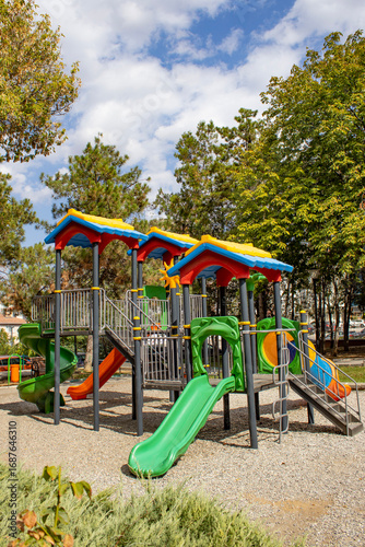 Wallpaper Mural Bright plastic playset with tunnel slide, spiral slide and seesaw in a green park. Useful for education, recreation, childcare brochure, urban planning article, parenting blog or safety guide. Torontodigital.ca