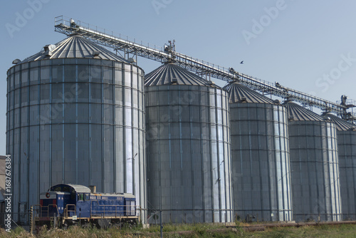 Grain storage silos and railroad car near large warehouse hangars at agricultural facility
