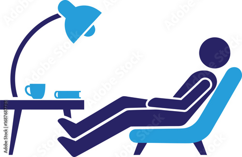 A person relaxing in a chair under a desk lamp with a cup and book on a nearby table.