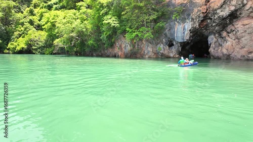 Tourists in canoeing enter a cave of a limestone cliff