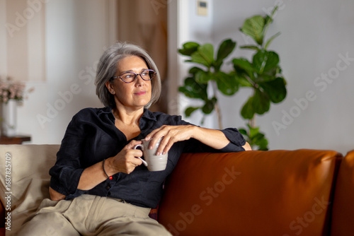 Senior woman relaxing on sofa with hot drink, enjoying domestic tranquility