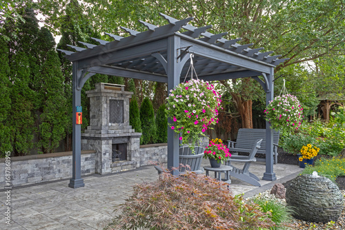 Wooden gray pergola on pavers with stone fireplace and waterfall urns landscape design idea for backyard sanctuary