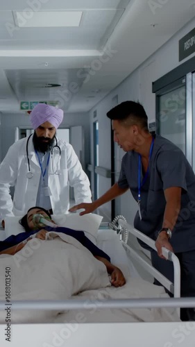 Vertical video: Diverse colleagues securing O2 mask and pushing stretcher down hallway to treatment
