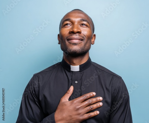 A dark-clad man of faith, hands placed on his chest, expresses profound devotion, gazing upward against a simple backdrop.