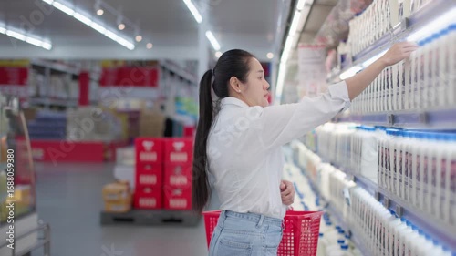 Asian woman browsing refrigerated dairy section in supermarket selecting carton of fresh milk, healthy grocery shopping choice, daily nutrition lifestyle, retail food market consumer experience