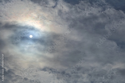 Fotografie Dramatic clouds partially cover the sun, creating a glow where the round shape of the sun is faintly visible from a distance, adding depth and atmosphere to the sky
