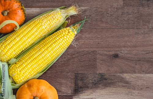 Autumn harvest. Small pumpkins and sweet corn are lying on wooden background. Top view.