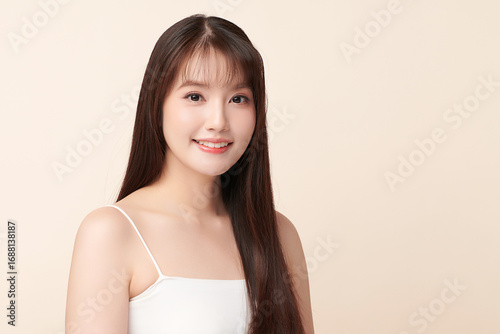 A beautiful young Asian woman with clean, fresh skin against a beige background. Skincare, facial treatment, cosmetology, beauty, and spa. An elegant portrait of an Asian woman.