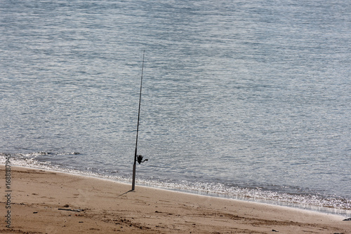 Fotografia Fishing rod stuck upright in the sand near the edge of the ocean at a beach