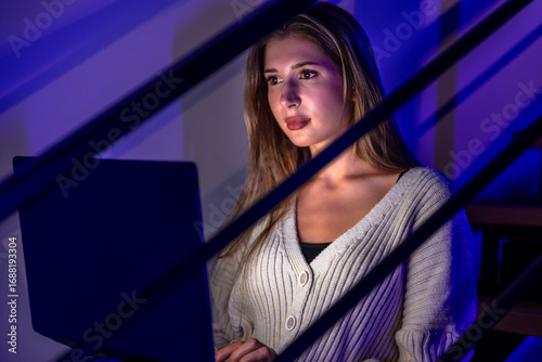 Young woman watching laptop under blue purple light. Close up.