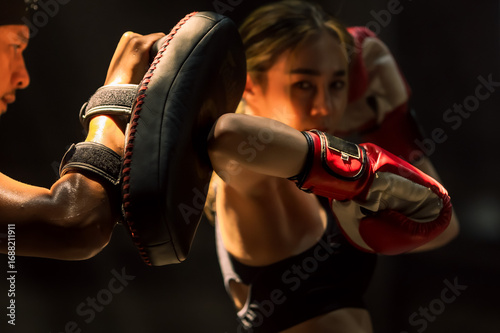 Confident female Muaythai boxer practicing Thai boxing with male trainer in gym