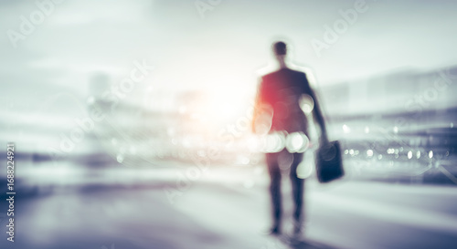 Businessman walking away carrying briefcase with city lights in the background.