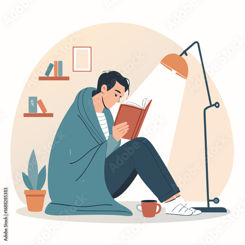 Young man wrapped in a cozy blanket reading a book at home.