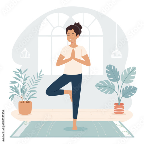 Young woman practicing tree pose yoga in a bright room.