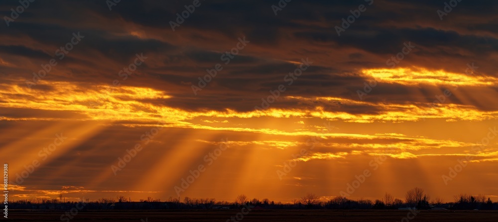 Fototapeta premium Golden sunset rays piercing dark clouds over a field