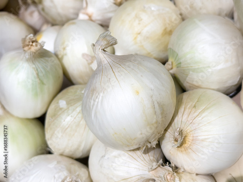 Fresh white onions close-up, piled together in a box, natural texture of bulbs, ideal for cooking, healthy eating, grocery sale, and vegetable background.
