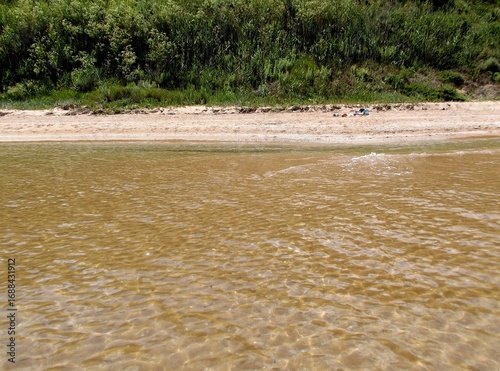 Transparent clear sea water of a sandy beach with green grass on background.