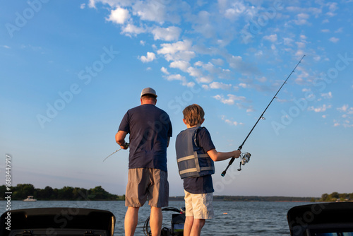 Father and son fishing together on a boat on a lake at sunrise