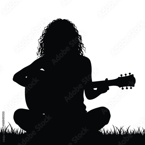 Silhouette of a person playing guitar sitting in grass