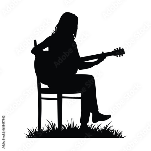 Silhouette of person playing acoustic guitar while sitting on chair in grass