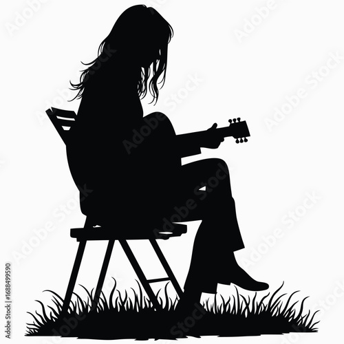 Silhouette of person playing guitar on chair in grass