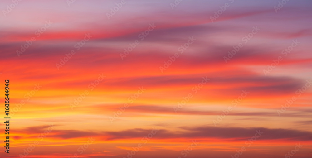 Obraz premium Colorful sky with clouds at sunset showing vibrant shades of orange and purple, creating a dramatic natural gradient with warm tones and a peaceful evening atmosphere.