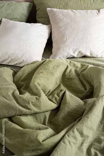Crumpled green bedding with white pillow on bed.