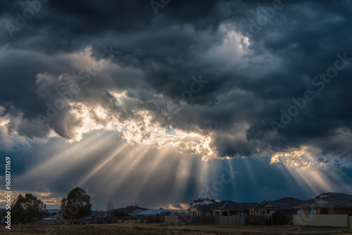 Sunbeams piercing a dramatic sky filled with dark clouds over a residential area
