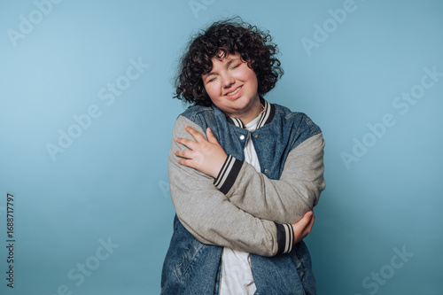 portrait of young woman wraps their arms around themselves, embodying self-love and comfort on blue background
