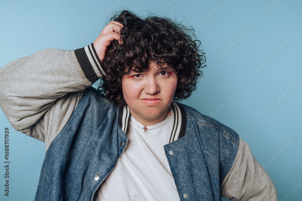 Obraz premium portrait of young woman scratches their head with a confused look, blending humor and a casual aesthetic in a lighthearted moment on blue background