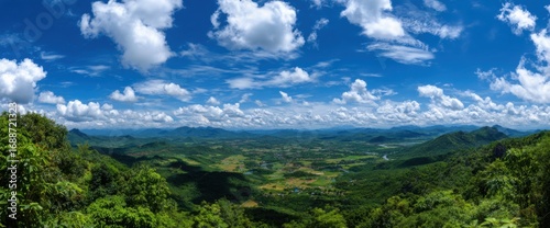 Panoramic view of lush green valleys and mountains under a vibrant blue sky dotted with fluffy white clouds