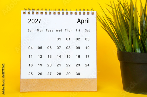April 2027 monthly desk calendar design with clean white layout, yellow background, and green plant decor