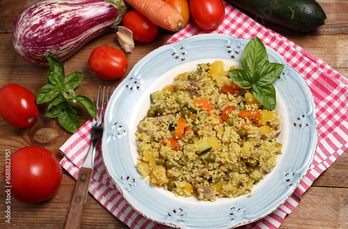 A plate of couscous with mixed vegetables and garnished with fresh basil leaves, photographed from above.
