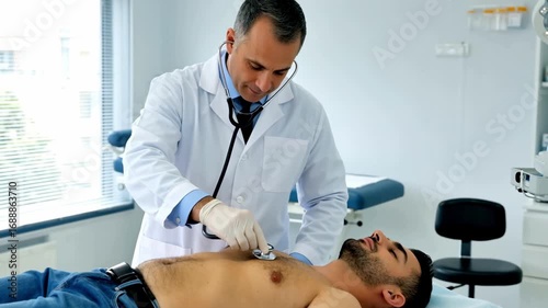 Professional European doctor examining shirtless male patient with stethoscope in modern medical clinic examination room