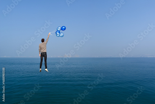 Canvas Print A boy flies over the sea, carried by balloons