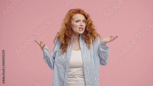 Confused red-curly haired woman shrugs shoulders showing uncertainty, confusion, hesitation