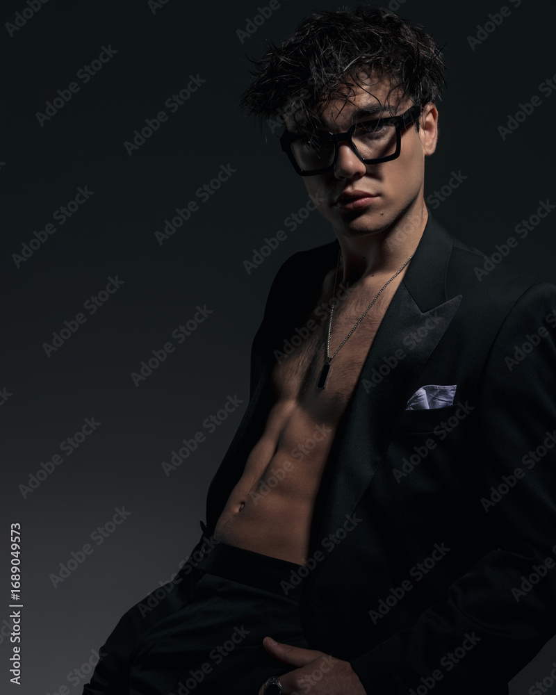 Obraz premium attractive fashion man with glasses showing abs muscles while sitting