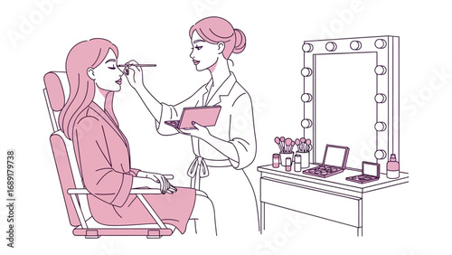 Artist applying makeup to a client in a chair with a lighted vanity mirror and beauty products nearby