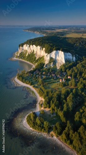 Scenic view from above showing a coastal area with chalk cliffs, trees, and a sandy beach on the shore under a sunny, blue sky