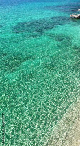 Crystal-clear turquoise water sparkles under the sun near a light-colored shoreline, suggesting a tranquil and inviting coastal scene