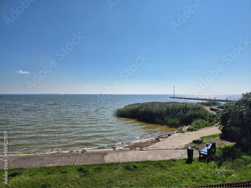 Wallpaper Mural "Scenic seaside view with calm blue water, a paved promenade, green grass, and a lone bench under a bright blue sky." Torontodigital.ca