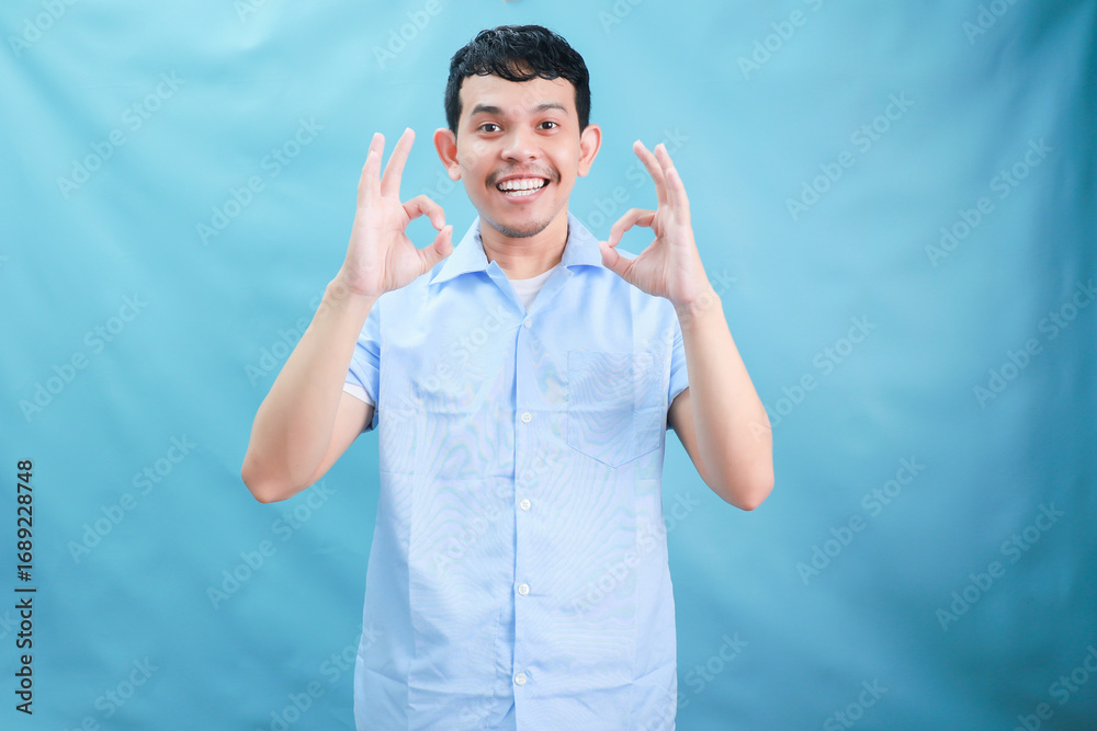 Naklejka premium Cheerful Young Man Giving a Positive Gesture in a Light Blue Background Delighting Viewers with His Smile