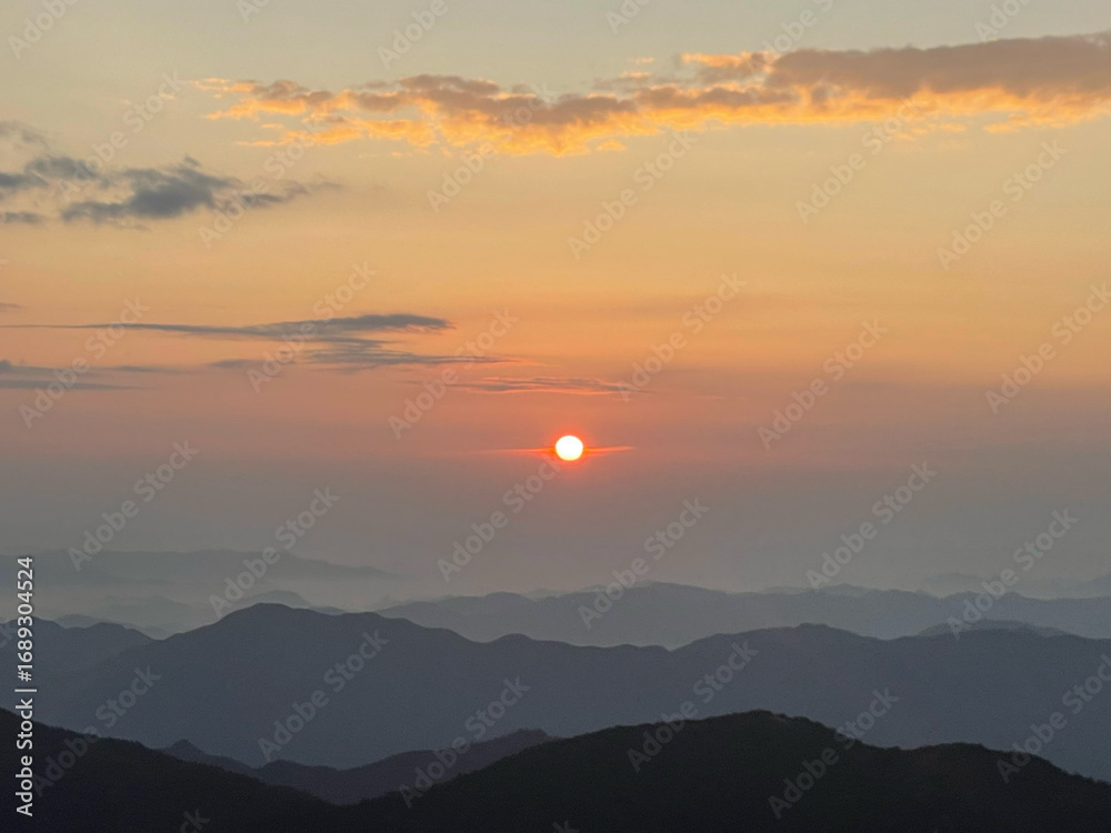 Fototapeta premium Warm sunlight bathing snow capped mountain ridges, golden light revealing layered peaks stretching across expansive wilderness landscape